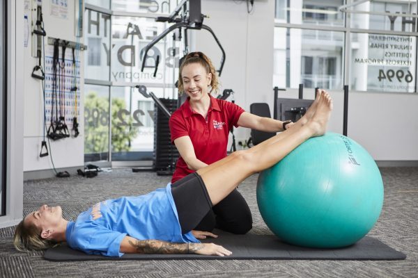 Alicia Cox, physiotherapist helping a patient with exercise using a large ball.