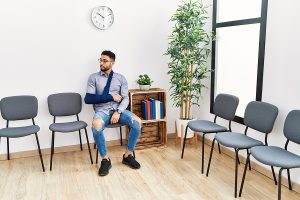 Young arab man sitting on chair with arm sling at physio clinic waiting